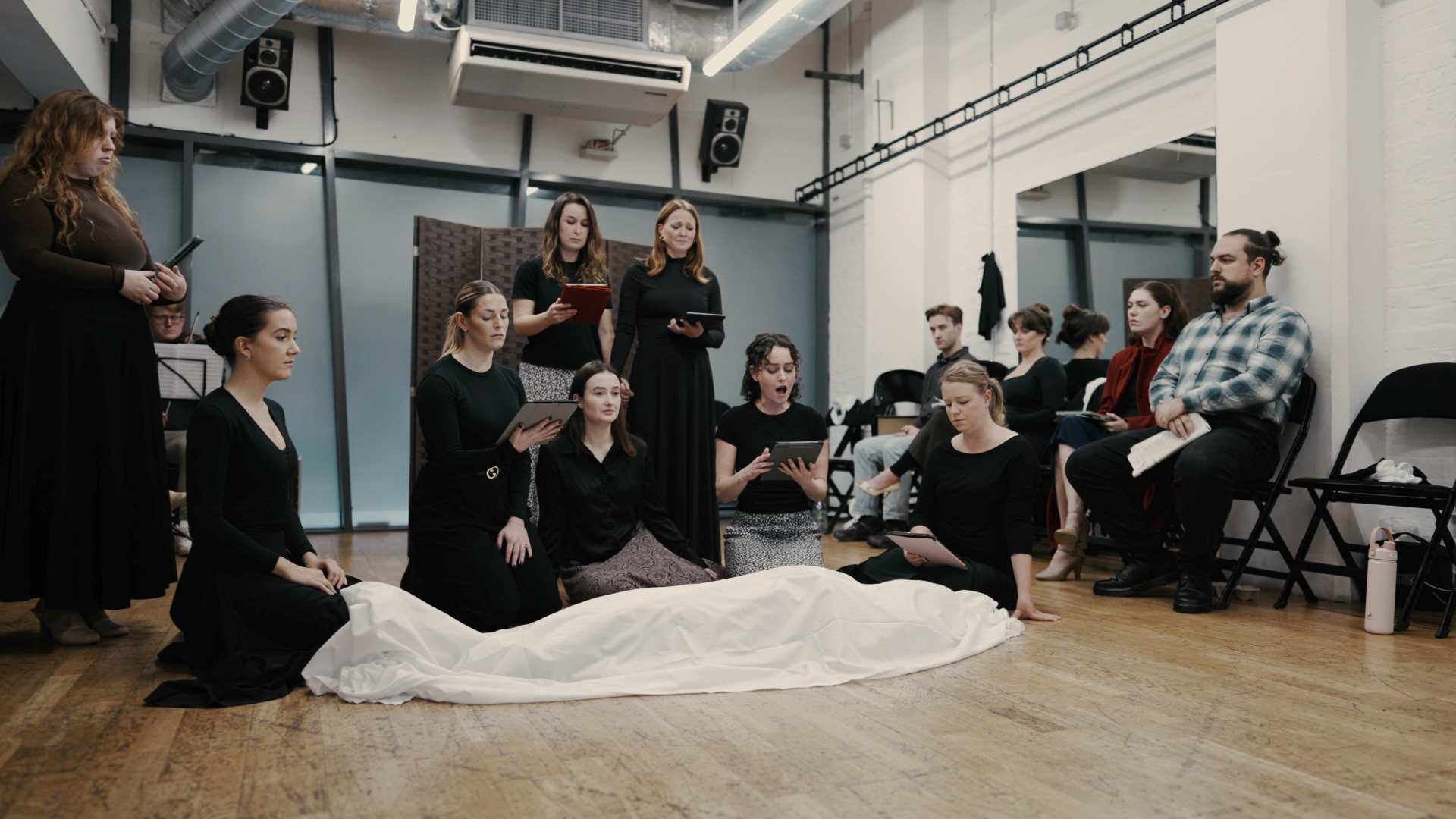 Ensemble scene with performers gathered around a shrouded figure